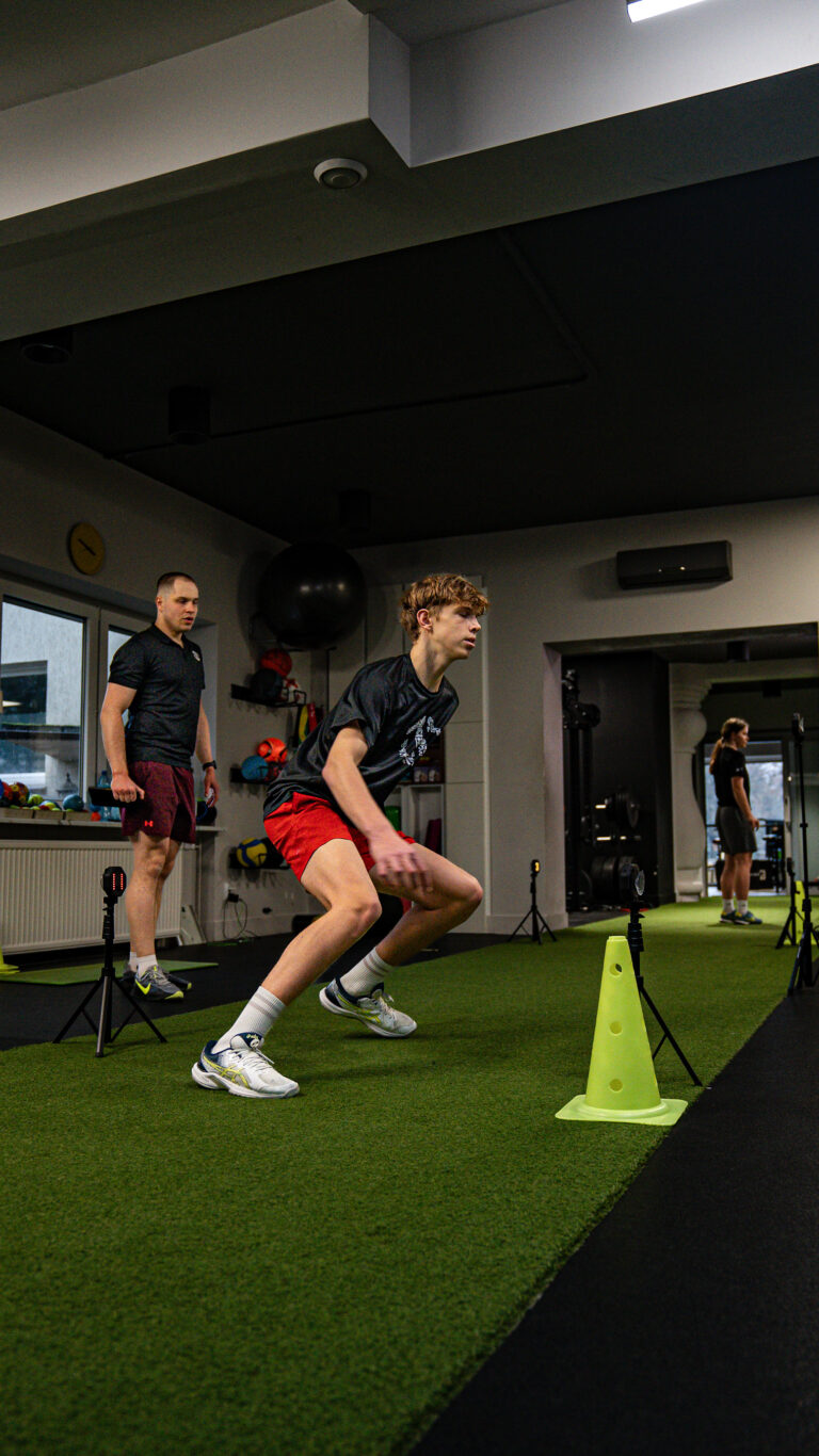 Zawodnik wykonujący test reakcji z wykorzystaniem fotokomórek w trakcie treningu motorycznego pod okiem trenera